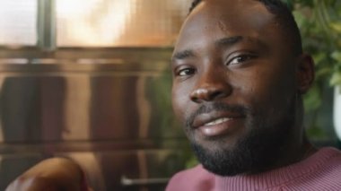 Kafede oturan, kameraya bakıp gülümseyen Afro-Amerikan bir adamın portresi.
