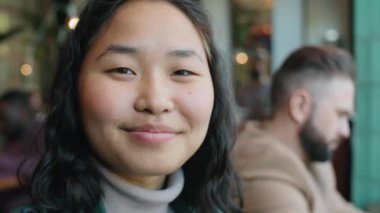 Kafede otururken kameraya bakıp gülümseyen mutlu Asyalı kadının portresi.