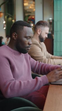 Kafe masasında oturan genç Afro-Amerikalı iş adamının dikey format görüntüleri.