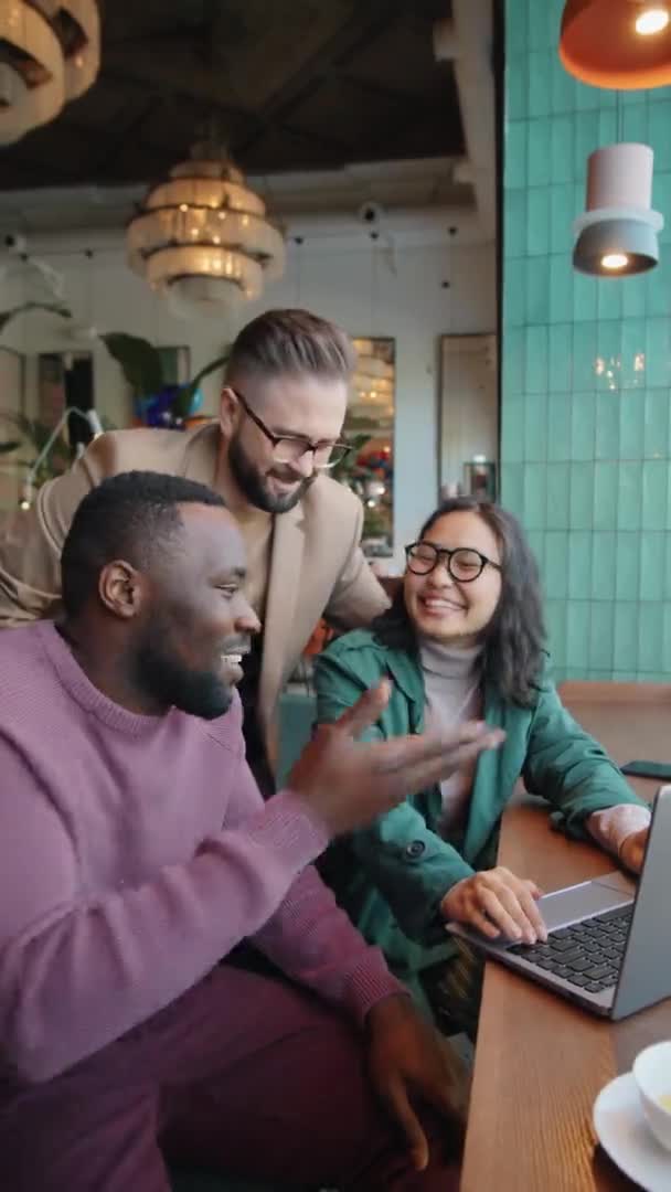 アフリカ系アメリカ人や白人男性の同僚と一緒にカフェで一緒に仕事をしながら 積極的なアジアのビジネス女性の笑顔とノートパソコンでプロジェクトを議論の垂直ショット — ストック動画