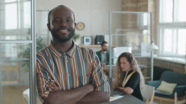 Kollarını kavuşturup gülümseyerek kameraya bakan, gündelik giyimli neşeli Afrikalı Amigo iş adamının belini kaldırın.