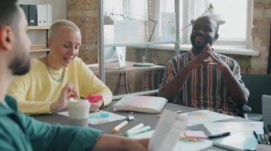 Tekerlekli sandalyede oturan ve çok ırklı iş arkadaşlarıyla konuşan engelli Afro-Amerikalı bir adam.