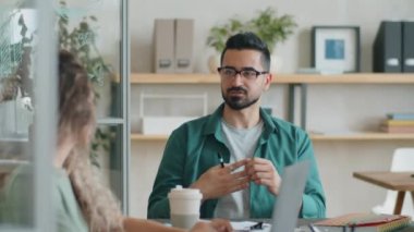Gecelik ve gözlüklü yakışıklı orta doğulu işadamı ofis toplantısı sırasında beyaz kadın meslektaşlarıyla tartışıyor.
