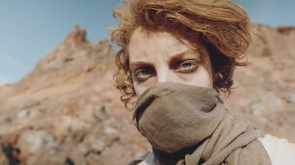 ポスト黙示録的な砂漠の中に立っている間 顔をカバーするスカーフを持つ若い女性の肖像アークショット — ストック動画