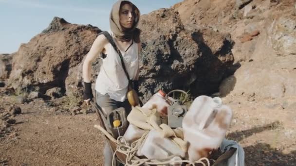 Jovem Mulher Roupas Velhas Empurrando Carrinho Com Latas Através Deserto — Vídeo de Stock