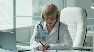 Laboratuvar önlüklü profesyonel bir kadın doktor bazı notlar yazıyor ve resepsiyonda çalışırken dizüstü bilgisayarda yazıyor.