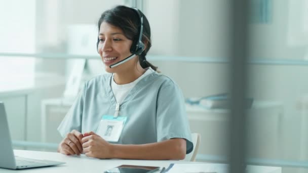 Hispanic Female Doctor Scrubs Wireless Headset Sitting Workplace Clinic Talking — Stock Video