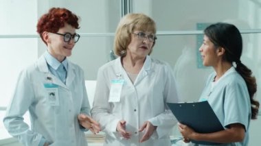Genç İspanyol hemşire ve iki beyaz kadın doktor konuşuyor ve sonra birlikte poz veriyorlar ve klinikte iş birliği yaparken gülümsüyorlar.