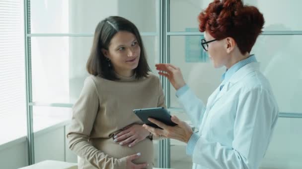 Pozitivní Žena Lékař Vysvětlit Něco Digitální Tablet Mluvit Těhotnou Ženou — Stock video