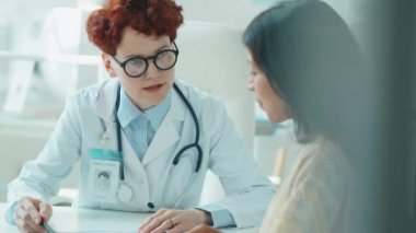 Genç beyaz kadın doktor panoda bir şey gösteriyor ve klinikte ona danışmanlık yaparken İspanyol kadınla konuşuyor.