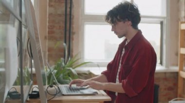 Genç Kafkasyalı iş adamı ofiste çalışırken bilgisayarı güneş paneliyle şarj ederken bilgisayar kullanıyor.