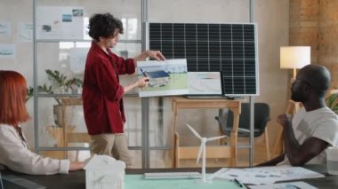 Alternatif enerji projesi hakkında sunum yapan Kafkasyalı genç mühendis ve çok ırklı meslektaşlarına güneş enerjisi bankasını gösteriyor
