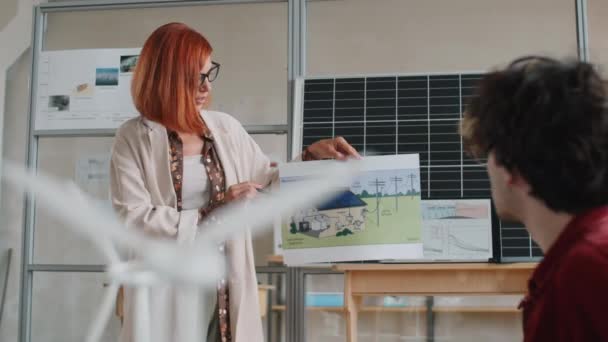 若い白人女性がオフィスの多民族男性の同僚に家の再生可能エネルギーシステムについて発表する — ストック動画