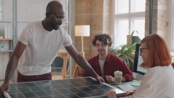 若いアフリカ系アメリカ人エンジニアがオフィスミーティングで太陽光パネルを持ち込み 白人の同僚と再生可能エネルギーソリューションについて話し合う — ストック動画