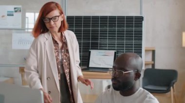 Kafkas kadın dizüstü bilgisayar kullanıyor ve yenilenebilir enerji şirketinde çalışırken Afrikalı-Amerikalı erkek meslektaşla bilgisayar üzerinde proje tartışıyor.