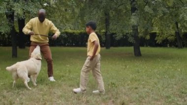 Tahta sopa tutan Afro-Amerikalı bir adam yeşil çimenlikte tatlı Golden Retriever köpeğiyle oynarken karısı ve küçük oğlu maçlarını izliyorlar.