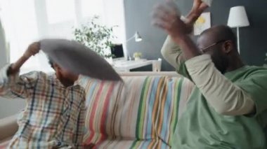 Heyecanlı afro-amerikan baba ve küçük oğlu evde oynarken kanepede yastık savaşı yapıyorlar.