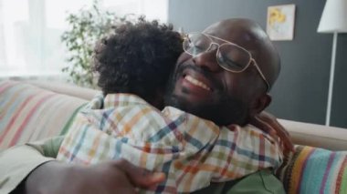 Küçük Afro-Amerikalı çocuk, mutlu babaya sevgiyle sarılıyor ve evdeki kanepede birbirine bağlanıyor.