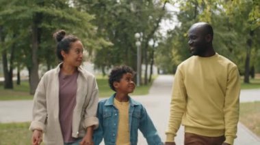 Mutlu Afro-Amerikan anne, baba ve küçük oğlu yaz günü parkta yürürken el ele tutuşup gülümsüyor ve sohbet ediyorlar.