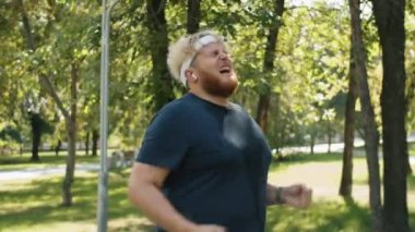 Yaz günü terli tişörtlü obez adam parkta koşuyor, sonra duruyor, akıllı adam izliyor ve yeni başarısını kutluyor.