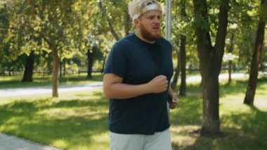 Spor giyim kuşağında terli obez adam yaz günü dışarıda egzersiz yaparken parkta koşuyor.