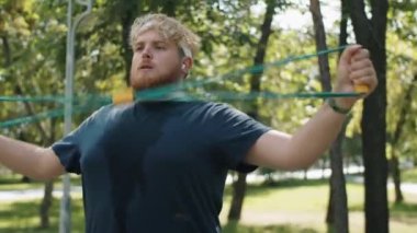 Spor giyim bölümünde terli, kilolu bir adam. Parkta yaz günü göğüs genişletme egzersizi yapıyor.