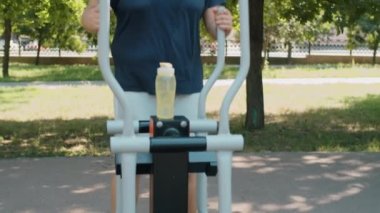Spor giyim kuşağında terli bir adamın yaz günü parkta yürüyüş makinesi üzerinde egzersiz yaparken çekilen pozu.