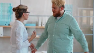 Kadın doktor, şişman adamın belini bant ile ölçüyor ve klinikte sağlık kontrolü sırasında ona danışmanlık yapıyor.