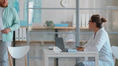 Obezite hastası bir adam klinikte yürüyor, kadın doktorlara tıbbi geçmişi veriyor ve onunla konuşuyor.