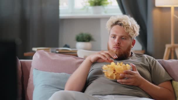 Joven Hombre Con Sobrepeso Sentado Sofá Casa Comiendo Papas Fritas — Vídeos de Stock