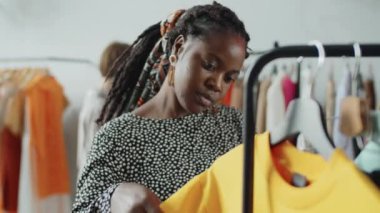 Genç ve güzel Afro-Amerikalı bir kadın elbise mağazasında giysilerini inceliyor.