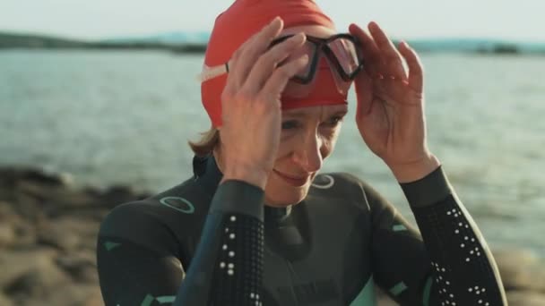 Жінка Триатлоністка Купальнику Кепці Одягає Окуляри Плавання Стоячи Березі Озера — стокове відео