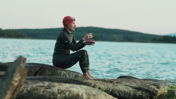 Żeński Triathlonista Stroju Kąpielowym Czapce Siedzący Skalistym Jeziorze Zdejmujący Gogle — Wideo stockowe
