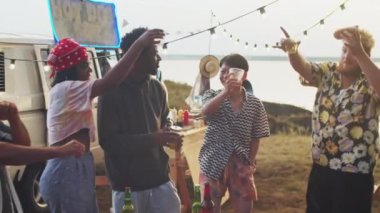 Neşeli, etnik çeşitlilikte arkadaşlar ellerinde içkiler, sokak yemekleri yiyip dans ediyorlar ve yaz festivalinde eğleniyorlar.