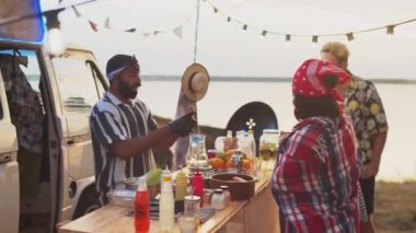 Neşeli orta doğulu satıcı yaz festivalinde yemek kamyonunda çalışırken sosisli sandviç pişiriyor ve çok ırklı müşterilerle sohbet ediyor.