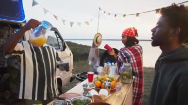 Orta Doğulu yemek kamyonu satıcısı yaz festivalinde çalışırken Afro-Amerikalı erkekler için plastik bardağa portakal suyu dolduruyor.