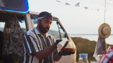 Tek kullanımlık eldivenli, sosisli sandviç pişiren ve yaz festivalinde yemek kamyonunda çalışırken insanlarla sohbet eden genç, pozitif bir Orta Doğulu satıcı.