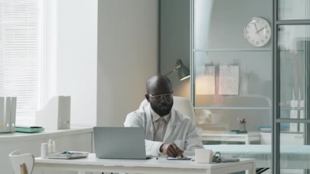 Médico Afroamericano Bata Laboratorio Gafas Trabajando Laptop Tomando Notas Escritorio — Vídeos de Stock