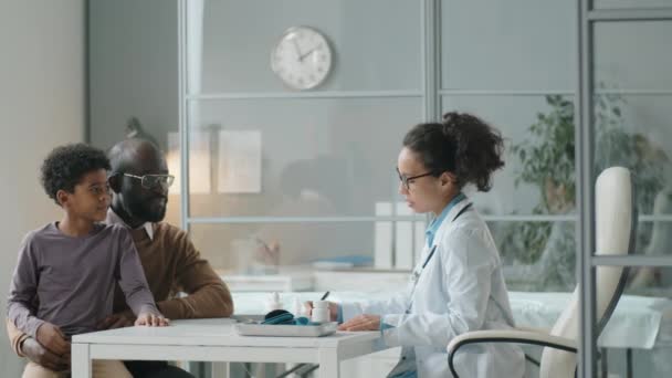 非洲裔美国男子与小儿子坐在医务室 在会诊期间与不同种族的女儿科医生交谈 — 图库视频影像