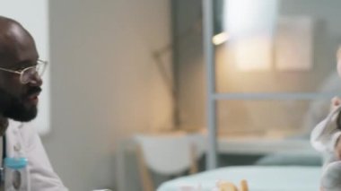 Güzel beyaz annesi klinikteki sağlık danışmanlığı sırasında Afrikalı Amerikalı çocuk doktoruyla konuşurken sevimli bebek oyuncakla oynuyor.