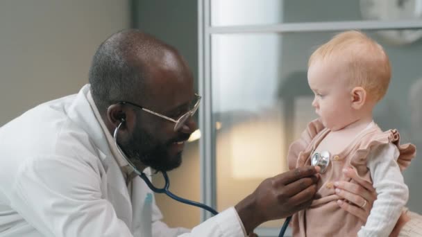 Veselá Běloška Drží Svou Dceru Zatímco Africký Americký Pediatr Kontroluje — Stock video