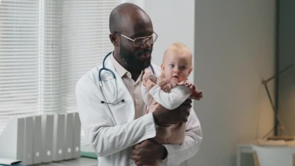 Šťastný Africký Americký Pediatr Drží Roztomilé Kavkazské Dítě Pažích Usmívá — Stock video