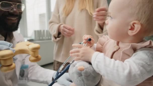 Adorable Niña Caucásica Sosteniendo Juguetes Jugando Con Alegre Médico Afroamericano — Vídeos de Stock