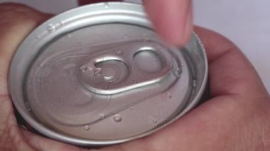 Yakından çekilen eller, içinde gaz olan alüminyum kahve konservesini hassas bir odak noktasıyla açıyorlar. Islak alüminyum teneke üzerine su damlacıkları.