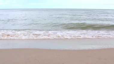 Gündüz vakti kumsalda deniz dalgaları esiyor. Dalgalar boş kumsala vuruyor.