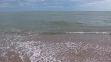 Gündüz vakti kumsalda deniz dalgaları esiyor. Dalgalar boş kumsala vuruyor.