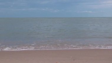 Gündüz vakti kumsalda deniz dalgaları esiyor. Dalgalar boş kumsala vuruyor.