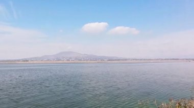 Huzurlu göl zumpangodur. Arka planda bir dağ ve kasaba manzarası vardır. Su rüzgarla hareket eder..