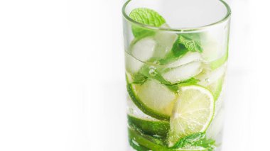 Beyaz arka planda, soğuk, yakın planda bir bardakta mojito kokteyli. Limon dilimleri, nane yaprakları ve buz küpleri..
