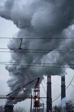 Fabrika boruları havayı kirletiyor, bacalardan çıkan duman, çevresel sorunlar, ekolojik tema, endüstri sahnesi. Dramatik gri sanayi manzarası.